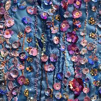 Glittering beaded curtain with pink and purple flowers, crystal droplets, and metallic chains creating magical light reflections on blue background. Decorative pattern.