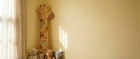 Wooden giraffe height measurement chart on nursery wall with stuffed animals below for child growth tracking and bedroom decoration.