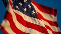 American flag waving in blue sky with stars and stripes displaying patriotic pride and national unity for Memorial Day Independence Day celebrations.
