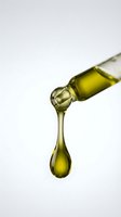 Golden olive oil drop falling from bottle spout on white background for culinary and cooking applications.