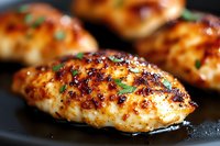 Juicy grilled chicken breasts with caramelized honey glaze and fresh herbs on black pan, close up view showing golden-brown crust and moist texture.