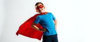 Young Caucasian boy in superhero costume with red cape and mask posing confidently against white background for children's costume and play concepts.