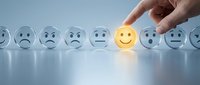 Hand selecting yellow smiley face among sad and neutral emoticons on white surface, representing positive attitude, customer satisfaction, mental health and emotional wellness concept.