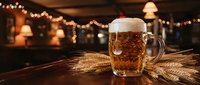 Frothy beer mug with golden lager on wooden table surrounded by wheat stalks in cozy pub atmosphere with warm bokeh lights for Oktoberfest celebration.
