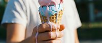 Person wearing white t-shirt holding melting ice cream cone with blue topping in sunny outdoor setting, ideal for summer, dessert, and food-related designs.
