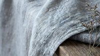 Soft gray linen fabric draped naturally with dried flowers creating cozy textile background for home decor and interior design projects.