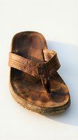 Worn brown leather thong sandal with distressed finish and natural patina, featuring adjustable strap and textured sole for casual footwear styling.