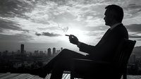 Silhouette of businessman smoking cigarette against dramatic sunset skyline, contemplative moment overlooking urban cityscape.