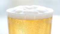 Chilled golden beer with thick white foam head and carbonation bubbles in clear glass on white background.