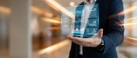 Businessman holding futuristic holographic tablet displaying data analytics charts and graphs in modern office corridor with motion blur background.