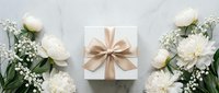 White gift box with beige ribbon surrounded by white roses and baby's breath flowers on marble background for special occasions and celebrations.