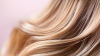 Smooth flowing blonde and brown hair strands with highlights creating elegant waves and texture against soft pink background, macro beauty shot.