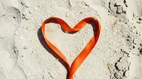 Red heart shape drawn in sandy beach surface with footprints and natural texture creating romantic summer love symbol for vacation memories.