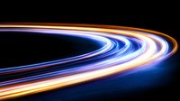 Glowing curved light trails in motion against dark background create dynamic streaks of blue, orange and white colors, suggesting speed and technology advancement.