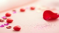 Red heart-shaped confetti and glitter scattered on soft pink background for Valentine's Day celebration, romance and love themed decorations.