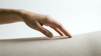 Hand gently touching soft white surface demonstrating tactile sensation and comfort for wellness and relaxation concepts.