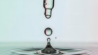 Water droplet falling and creating ripples on calm surface with soft gradient background for wellness and purity concepts.