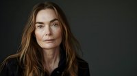 Portrait of mature woman with long auburn hair against dark background, wearing black shirt, conveying confidence and contemplation.