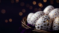 White Easter eggs decorated with golden metallic patterns and dots on dark background with bokeh lights and purple flower petals, festive holiday composition.