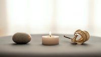 Zen meditation setup with burning candle, smooth stone and wooden honey dipper on dark surface creating peaceful spa atmosphere for relaxation and mindfulness.