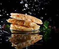 Stacked pancakes with water drops splashing and reflection on black background, garnished with mint leaves and pomegranate seeds, dramatic food photography.