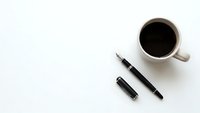 Black coffee cup with fountain pen and ink cartridge on white background for business writing and office workspace concepts.