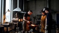 Two skilled blacksmiths working with glowing hot metal in traditional forge workshop with anvil and tools for metalworking craftsmanship education.