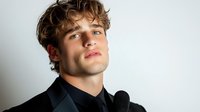 Young Caucasian male performer in black formal attire holding microphone against white background, expressing confidence and charisma for entertainment and music industry.