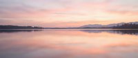 Serene lake at dawn with pink and purple sky reflecting on calm water surface, mountains in distant background, peaceful nature landscape.