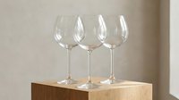 Three elegant crystal wine glasses arranged on wooden surface against neutral background for dining and entertaining occasions.