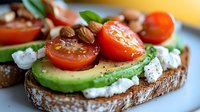 Fresh avocado toast with cherry tomatoes, crumbled feta cheese, almonds and basil leaves on rustic bread, seasoned with black pepper and sea salt.