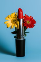 Red lipstick with yellow and red gerbera daisies against blue background, creative beauty and cosmetics composition for makeup and skincare marketing.