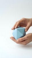 Hands gently holding light blue geometric paper origami shape against clean white background for creative design projects.