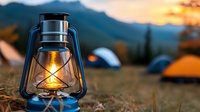 Vintage camping lantern glowing at sunset with mountain backdrop and tents. Outdoor adventure, hiking, wilderness exploration concept for travel designs.