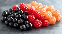 Fresh assorted berries arranged in rows - black currants, red raspberries, and golden raspberries on dark background with selective focus and soft lighting.