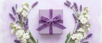 Purple gift box with satin ribbon surrounded by fresh lavender and white flowers on soft lilac background for special occasions and celebrations.