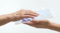 Mature woman handing transparent credit card to younger woman's hand against white background, representing financial transaction, payment processing, banking services, and money transfer.