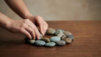 Hands arranging smooth river stones on wooden surface for meditation, spa therapy, wellness practices, and mindful relaxation activities.