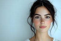Young Caucasian woman with natural makeup and messy bun hairstyle looking at camera against white background for beauty and skincare concepts.