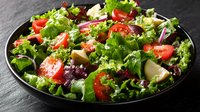 Fresh mixed green salad with tomatoes, cheese and vegetables served on black plate for healthy dining and nutrition.