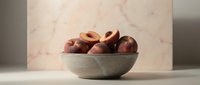Fresh ripe stone fruits in ceramic bowl against marble background, suitable for food styling, culinary blogs, recipe websites, and healthy eating content.