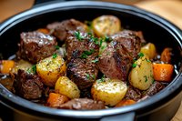 Tender beef stew chunks with golden potatoes and carrots in black ceramic pot, garnished with fresh herbs, slow-cooked to perfection in savory sauce.