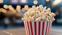 Fresh popcorn overflowing in classic red and white striped container against blurred bokeh background, creating nostalgic cinema atmosphere.