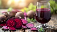 Fresh beetroot juice in glass with sliced raw beets on rustic wooden table. Healthy detox drink rich in antioxidants and vitamins for wellness lifestyle.