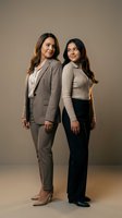 Two confident Latina women, adult and teen, posing back to back in stylish neutral outfits against a warm beige studio background.