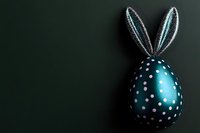 Metallic turquoise Easter egg decorated with white polka dots and silver bunny ears on dark green background with copy space for seasonal greeting.