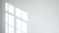 Sunlight streaming through window panes creates geometric shadows on minimalist white wall, ideal for backgrounds and design projects.