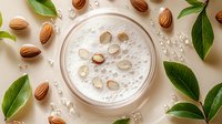 Creamy almond milk smoothie with fresh nuts and green leaves on beige background. Scattered almonds and bubbles create natural composition for healthy lifestyle.