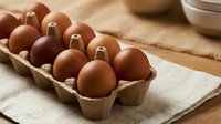Fresh brown eggs in cardboard carton on rustic wooden table with natural linen cloth, organic farm produce ready for cooking and baking recipes.