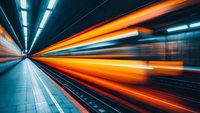 Long exposure shot of subway platform with dynamic motion blur creating orange and blue light trails against dark tunnel background, conveying speed and urban movement.